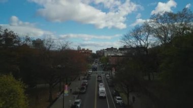 Şehir mahallesindeki caddenin üzerinde ilerliyorlar. Ağaçlarla ve apartmanlarla dolu yolda giden arabalar. New York City, ABD.