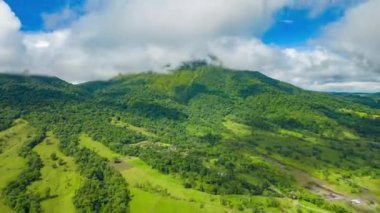 İleri, vahşi arazinin üzerinde uçar. Yeşil ağaçlık tepelerin üzerinde hareket eden yüksek hızlı bulutlar görüntüsü. Kosta Rika.