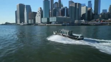 Yörünge, East River 'da hızla giden küçük bir motorlu teknenin etrafında çekildi. Aşağı Manhattan 'daki iş binaları ve arka planda ünlü köprüler. New York City, ABD.