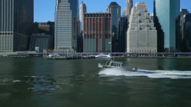 Güneşli bir günde Metropolis 'teki yüksek binalar boyunca nehirden geçen motorlu teknenin yan takibi. New York City, ABD.