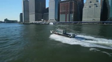Şehirdeki su yüzeyinde küçük bir tekne hızla hareket ediyor. Rıhtımdaki yüksek katlı iş binaları. New York City, ABD.