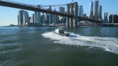 Brooklyn Köprüsü 'nün altından geçen tekneyi takip ediyoruz. Arka planda Aşağı Manhattan 'daki ikonik gökdelenler var. New York City, ABD.