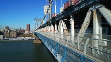 Parlak güneş tarafından aydınlatılan Manhattan Köprüsü 'nün devasa çelik inşaatı boyunca ileriye doğru uçar. Alt güvertede metro treni sürüyor. New York City, ABD.