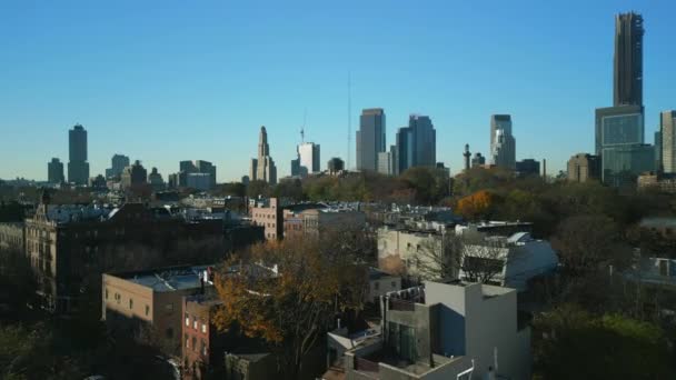 前方住宅街区の町の開発の上を飛ぶ 背景に澄んだ青空に対する近代的な高層オフィスタワー 米国ニューヨーク市 — ストック動画