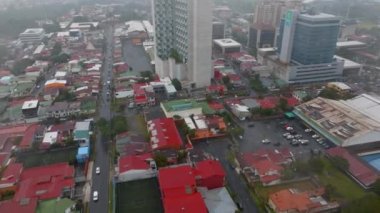 Forwards fly above buildings in town. Colour low houses and modern concrete tall buildings. San Jose, Costa Rica.