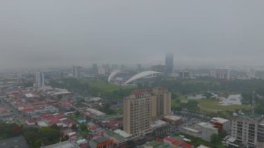 Forwards fly above urban borough. La Sabana Park with Estadio Nacional de Costa Rica. Aerial misty view of city. San Jose, Costa Rica.