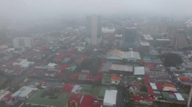 Forwards fly above colour roofs on town development on rainy day. Low clouds above capital. San Jose, Costa Rica.