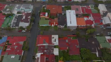 Fly above colourful roofs on low houses in residential neighbourhood. High angle aerial view of town development on rainy day. San Jose, Costa Rica.