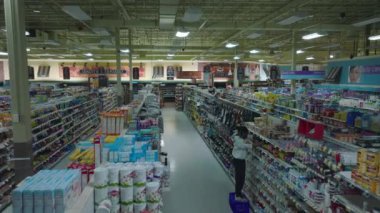 Dimmed lights in shop after closing hours. Worker replenishing and arranging products on shelves. Interior of large supermarket outside opening hours.