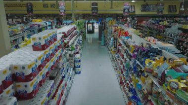 Forwards fly above empty aisle between shelves with goods in shop. Interior of large supermarket outside opening hours.