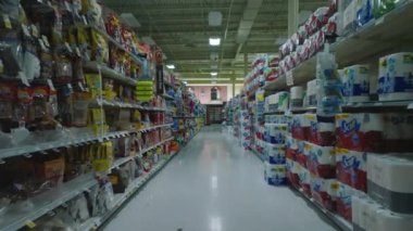 Forwards fly in aisle between goods arranged on shelves in empty shop. Interior of large supermarket outside opening hours.