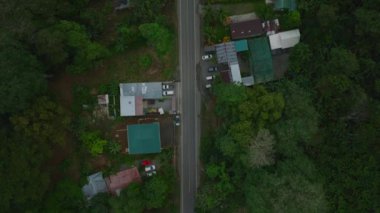 Flying over urban houses and streets in a suburban area of a settlement in the forest. Residential district with buildings and streets in lush green landscape