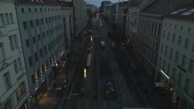 Forwards fly above street in city at dusk. wide road with tram tracks lined by multistorey buildings. Berlin, Germany.