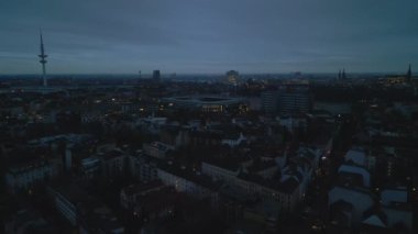Forwards fly above urban borough at twilight. Millerntor Stadion and TV tower silhouette against sky. Hamburg, Germany.