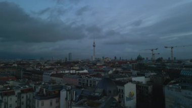 Aerial panoramic view of cityscape at dusk. Famous tall Fernsehturm and cranes towering above town development. Descending footage. Berlin, Germany.