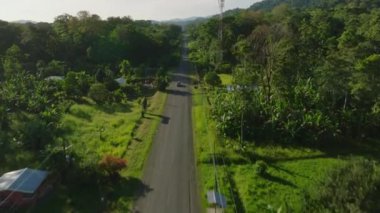 Aerial view of highway crossing forest in a urban settlement. Flying over a street meandering the lush rainforest