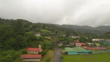 Fly above village in tropical destination in rainy weather. Buildings and roads surrounded by green vegetation. La Fortuna, Costa Rica.