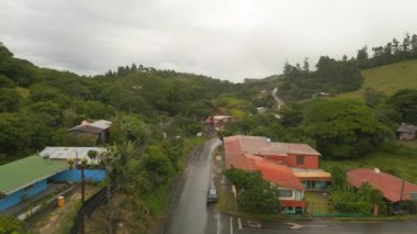 Forwards fly above wet road leading through poor village in tropical countryside. La Fortuna, Costa Rica.