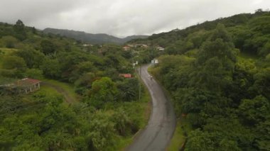 Forwards fly above landscape, man riding motorbike on road and passing village. La Fortuna, Costa Rica.
