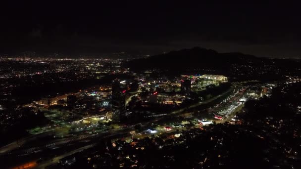 有名なユニバーサルシティの建物や周りをリード忙しい高速道路の空中パノラマ映像 夜の町の開発 米国カリフォルニア州ロサンゼルス — ストック動画