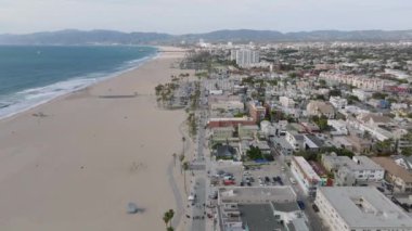 Venedik sahilinin havadan panoramik görüntüsü. Geniş kum kaplı okyanus kıyıları ve şehir merkezindeki binalar. Los Angeles, Kaliforniya, ABD.