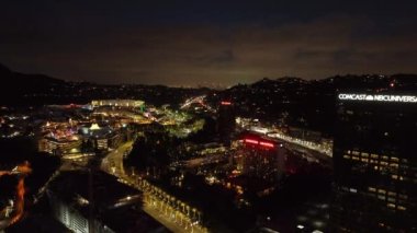 Geceleri Universal City 'deki aydınlık sokakların ve binaların hava görüntüleri. Modern yüksek binalar ve otoyol çevrede dolanıyor. Los Angeles, Kaliforniya, ABD.