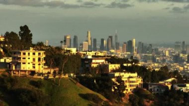 Şehrin tepelerindeki zengin yerleşim bölgesindeki gayrimenkullerin üzerinden uç. Arka planda modern yüksek gökdelenler var. Los Angeles, Kaliforniya, ABD.