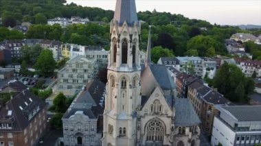 Yüksek kuleli Heilig Kreuz Kirche. Geriye doğru şehirdeki binaları ve arka plandaki ağaçlık tepeleri gösteriyor. Aachen, Almanya.