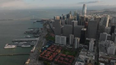 Sahilde gökdelenleri olan bir iş merkezi. Su yüzeyine yayılan büyük asma köprü. Metropolis 'in altın saatindeki hava manzarası. San Francisco, California, ABD