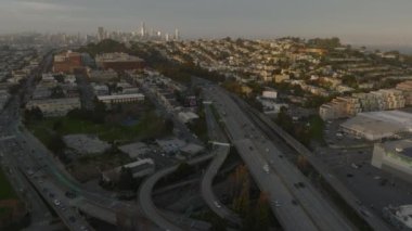 Gün batımında kalabalık şehirli mahallelerindeki kalabalık otoyolun ve kavşakların üzerinden uç. Uzakta gökdelenler olan bir gökyüzü. San Francisco, California, ABD