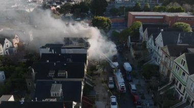 Şehir merkezindeki caddenin yukarısına uç. İtfaiyeciler yanan evle kavga ediyor. Alevden yükselen kalın duman. San Francisco, California, ABD