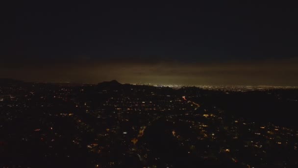 夜の街の空中降下映像 住宅街区と丘の後ろに輝く大都市 米国カリフォルニア州ロサンゼルス — ストック動画
