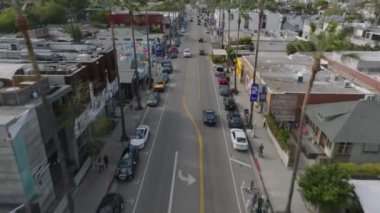 Uzun palmiye ağaçlarıyla kaplı caddede giden araçların izini sürüyorum. Venedik şehir merkezindeki yol boyunca binalar. Los Angeles, Kaliforniya, ABD.