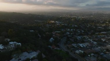 Gün batımında şehir merkezindeki evlerin hava panoramik görüntüleri. Şehrin tepelerindeki konutların üzerinden geriye doğru uç. Los Angeles, Kaliforniya, ABD.