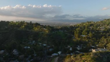 Şehir çevresindeki evlerin üzerinden ileriye doğru uçuyor. Öğleden sonra bir sürü yeşillik olan Hilly manzarası. Los Angeles, Kaliforniya, ABD.