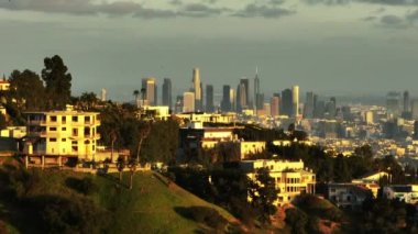 Şehrin tepelerindeki zengin yerleşim bölgesindeki gayrimenkullerin üzerinden uç. Arka planda modern yüksek gökdelenler var. Los Angeles, Kaliforniya, ABD.
