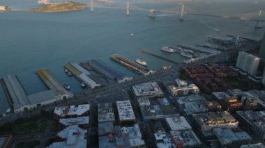 Sahildeki rıhtımların havadan kayma ve pan görüntüleri. Bay Bridge arka planda. San Francisco, California, ABD