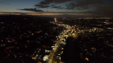 İleri, akşam şehrinin üzerinde uçar. Alacakaranlık Gökyüzü 'nün altında, kentsel mahallede aydınlık ve yoğun bir bulvar. Los Angeles, Kaliforniya, ABD.