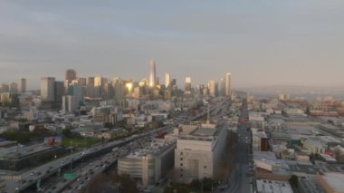 Metropolis 'teki şehir merkezinin üzerinde ilerliyorlar. Günbatımını yansıtan parlak cepheli modern gökdelenler. Çok şeritli yollarda yoğun trafik var. San Francisco, California, ABD