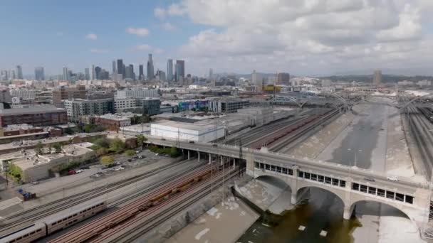 鉄道線路やコンクリート川運河にまたがる道路橋の素晴らしい空撮 背景に高層ビルのダウンタウン 米国カリフォルニア州ロサンゼルス — ストック動画