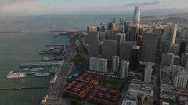 Sahilde gökdelenleri olan bir iş merkezi. Su yüzeyine yayılan büyük asma köprü. Metropolis 'in altın saatindeki hava manzarası. San Francisco, California, ABD