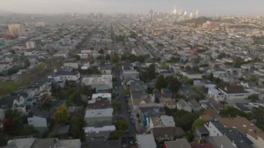Şehirdeki yerleşim yerlerindeki sıra sıra aile evlerinin hava panoramik görüntüleri. Şehir merkezindeki gökdelenlerin olduğu bir gökyüzü. San Francisco, California, ABD