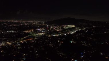 İleri, gece şehrinin üzerinde uçar. Universal City 'deki aydınlık binaların etrafında çok şeritli otobanda giden arabalar. Los Angeles, Kaliforniya, ABD.