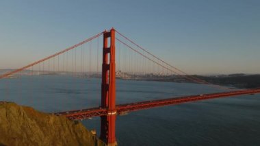 Büyük asma köprü kulesinin altın saatinde havadan kayma ve pan görüntüleri. Golden Gate Köprüsü 'nde trafik ve arka planda şehir. San Francisco, California, ABD.
