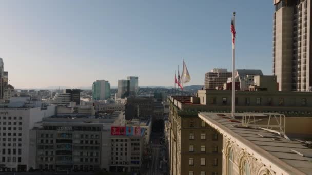 進む歴史的なホテルの屋根の上にフラグに沿って飛ぶ 市内中心部の建物の空中ビュー 米国カリフォルニア州サンフランシスコ — ストック動画