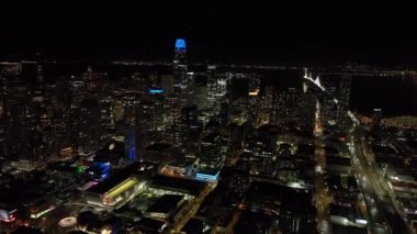 İleri, Metropolis 'in üzerinde uçuyor. Pencereleri ışıklandırılmış yüksek katlı ofis binalarının manzarası. Mavi kapaklı Satış Gücü Kulesi. San Francisco, California, ABD.