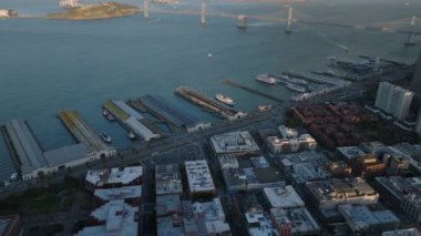 Sahildeki rıhtımların havadan kayma ve pan görüntüleri. Bay Bridge arka planda. San Francisco, California, ABD