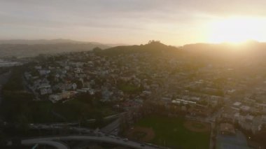 Güneşin batışına karşı tepelik arazideki banliyölerin hava panoramik görüntüleri. Şehirdeki konut ve ulaşım altyapısı sıraları. San Francisco, California, ABD