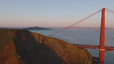 Golden Gate Köprüsü 'ndeki kıyı kayalıklarının üzerinden uçun. İnsanlar altın saatinde ünlü köprü manzarasının keyfini çıkarıyorlar. San Francisco, California, ABD.