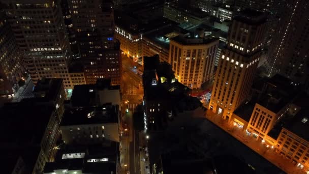 夜の街の上を飛ぶ 下の車の道路の交差点を通過する上で傾き ライトアップされた通りや高層オフィスビル 米国カリフォルニア州サンフランシスコ — ストック動画